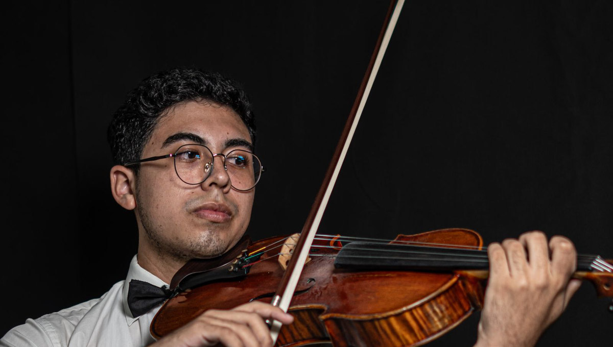 Violinist with his complete face visible, performing against a dark background (illustrative stock photo)