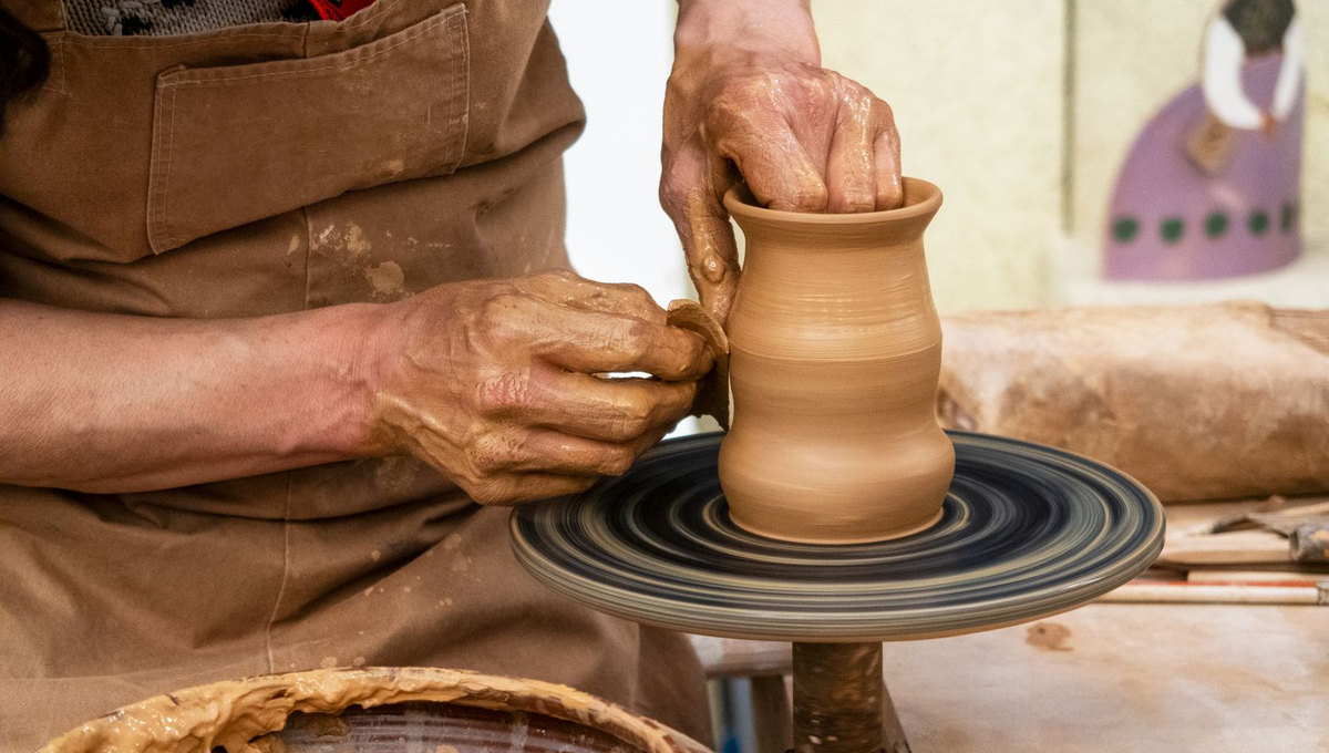 Close-up of hands shaping a clay vessel on a pottery wheel (illustrative stock photo)
